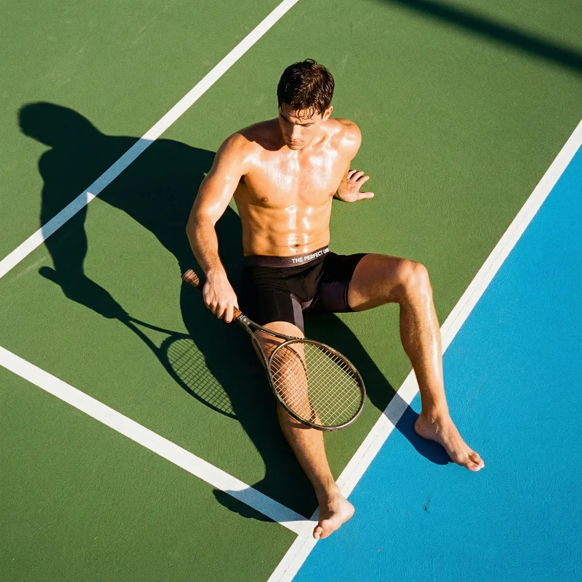 The Perfect Underwear bamboo boxer briefs in black, shown worn on a male model on an outdoor tennis court holding a racket.